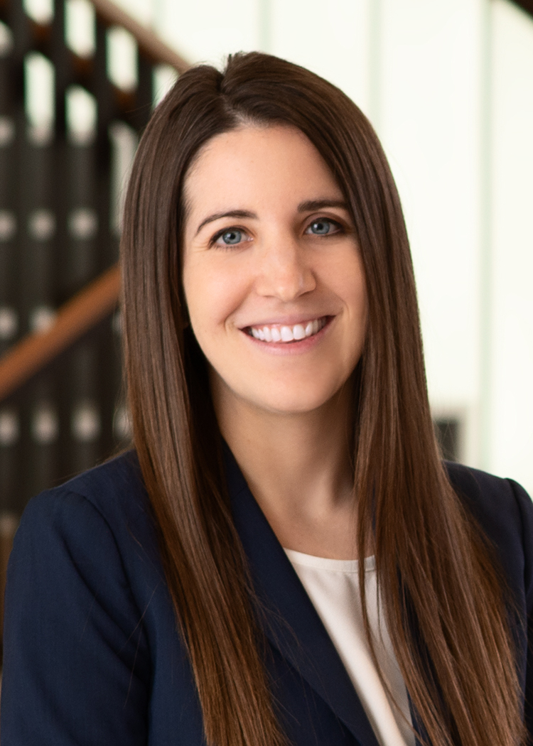 Professional up close headshot of Cody Wolpert in a navy suit and white blouse with stairs in the background