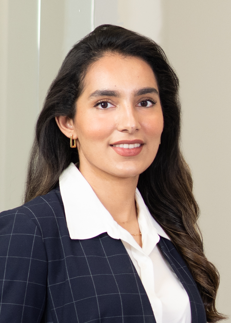 Close-up headshot of Kanwal S. Awan, standing in an office. Wearing a dark blazer with a white collared shirt