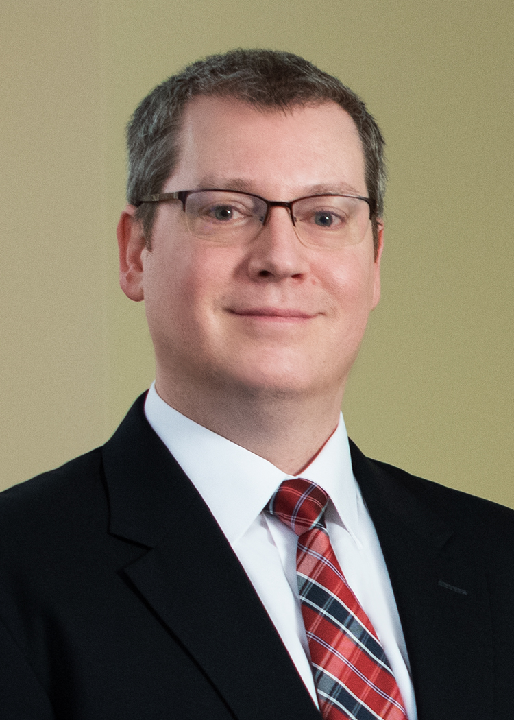 Close-up headshot of William Buchanan. Wearing a black suit with a white button down shirt and red tie.